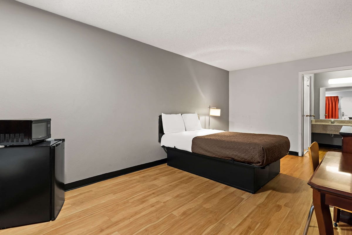 A compact hotel room with a bed, a desk, a microwave, and a small kitchenette.