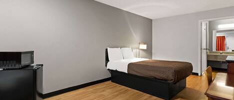 A compact hotel room with a bed, a desk, a microwave, and a small kitchenette.