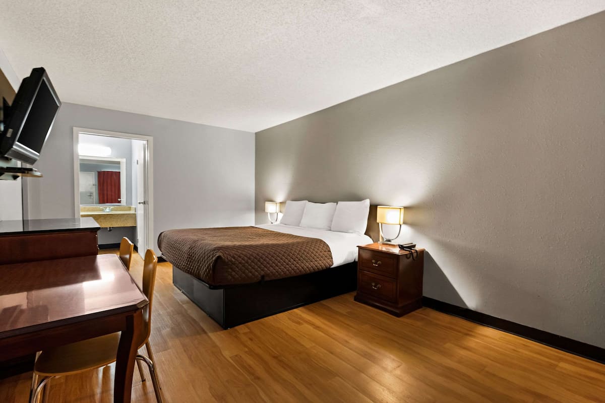 A bedroom with a bed, bedside table, lamp, wooden desk, and chair.