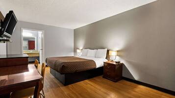 A bedroom with a bed, bedside table, lamp, wooden desk, and chair.