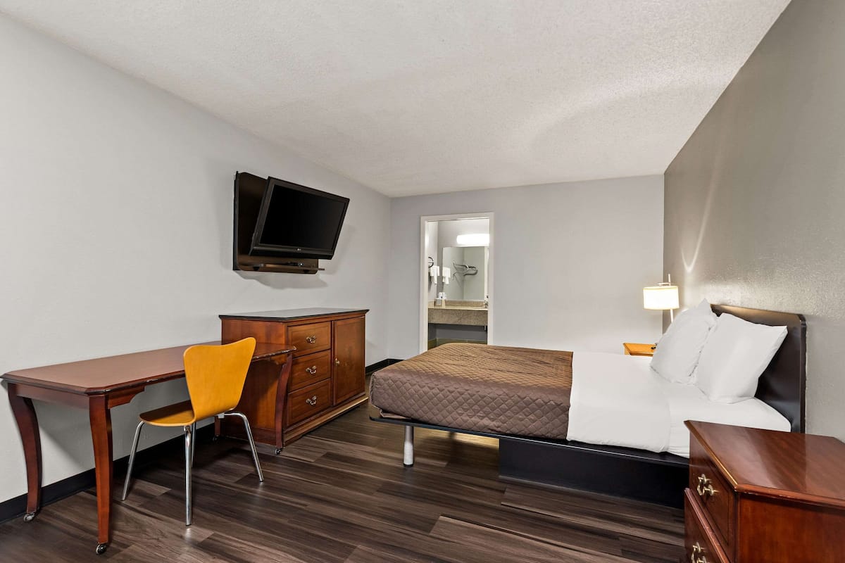 A hotel room with a bed, a desk, a chair, a TV, a dresser, and a mirror.
