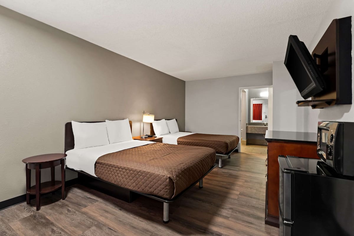 A hotel room with two beds, a TV, a small table, and a kitchenette.