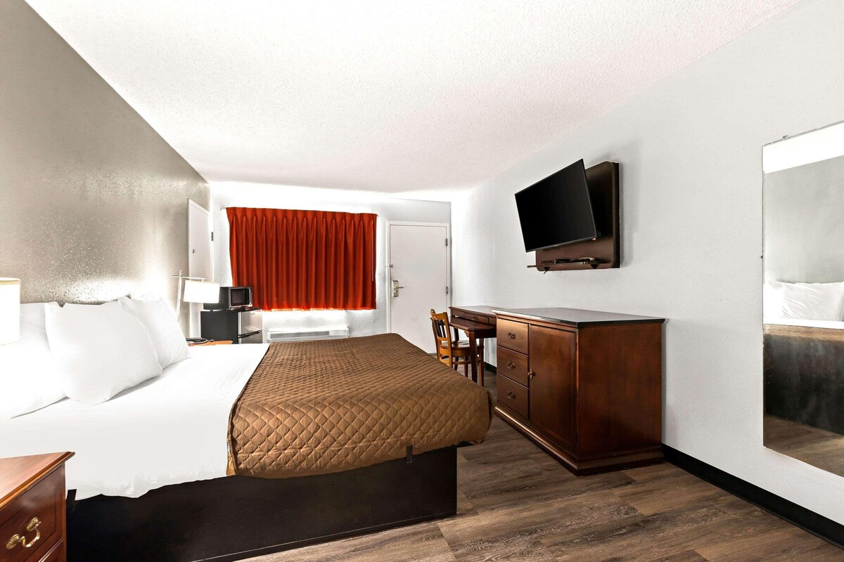A hotel room with a bed, a desk, a chair, a TV, and a wardrobe.