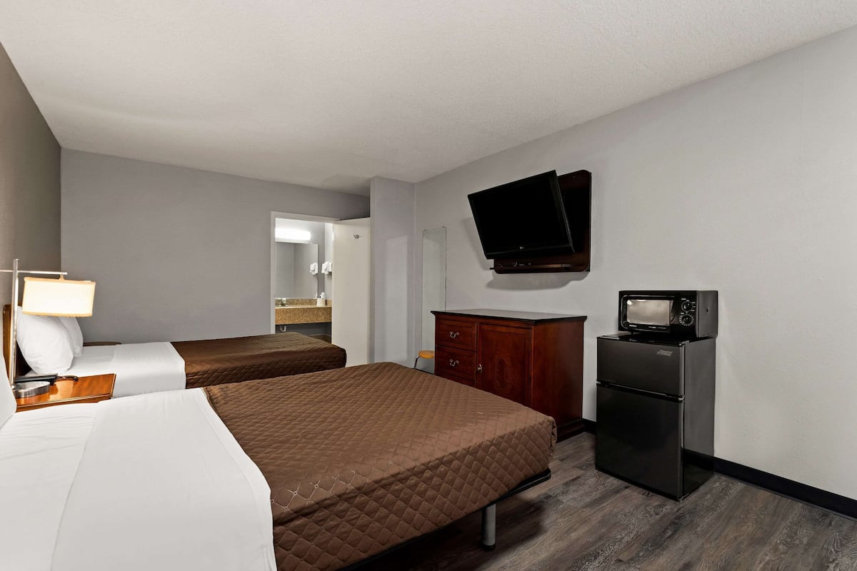 A hotel room with two beds, a TV, a refrigerator, and a wooden cabinet.