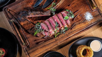 Een steak op een houten plank met een mes en een fles.