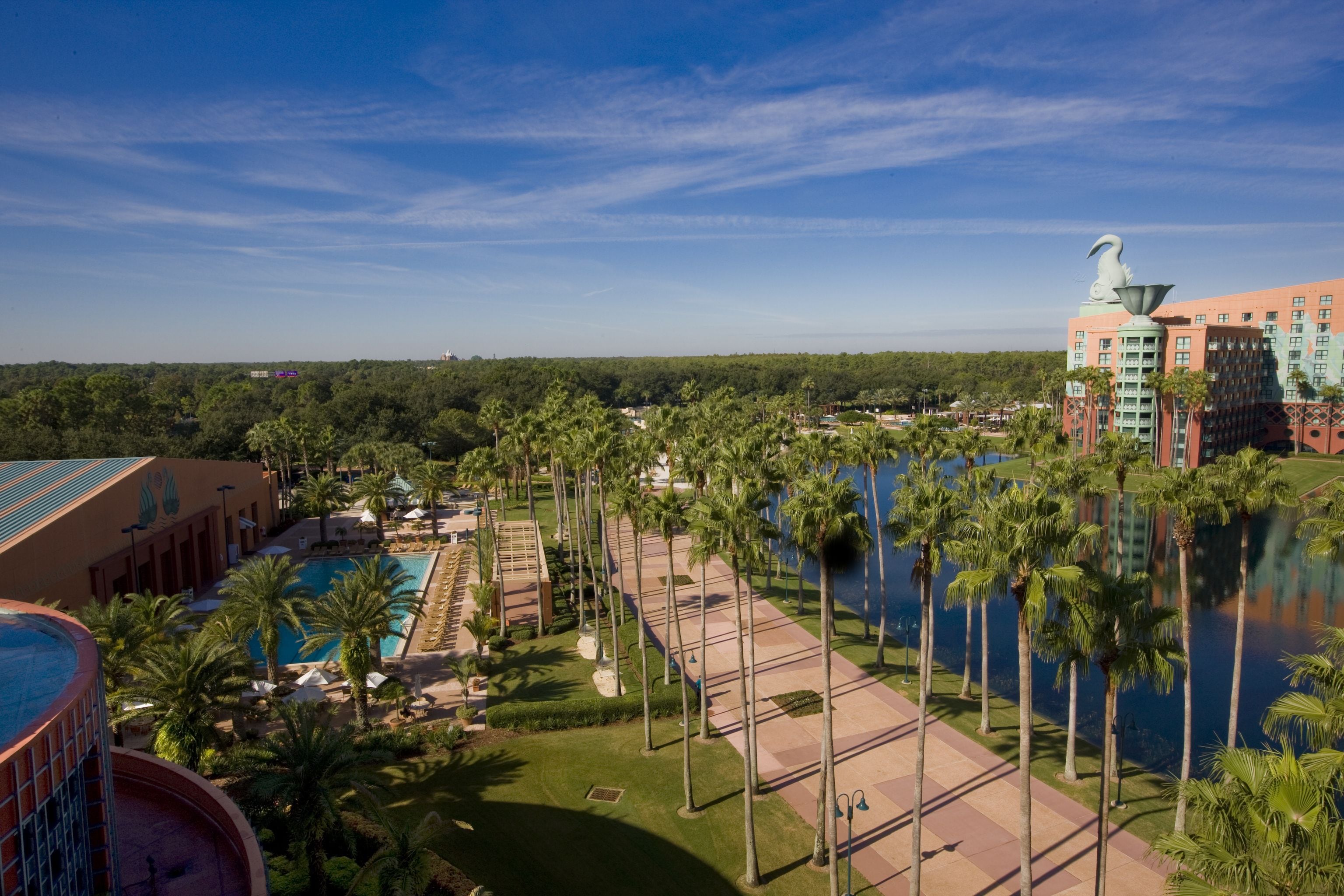 A resort with a pool, palm trees, and a large building with a distinctive sculpture.