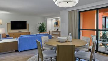 A modern living room with a round dining table, blue sofa, and a flat-screen TV mounted on the wall.