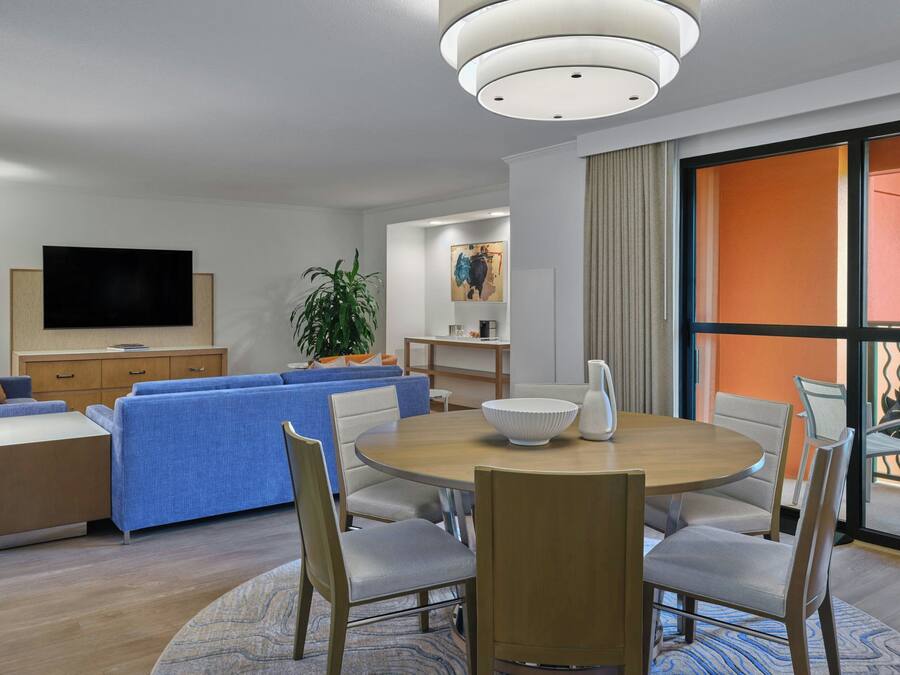 A modern living room with a round dining table, blue sofa, and a flat-screen TV mounted on the wall.