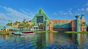 A large hotel with a pyramid-shaped building, a boat on the water, and palm trees. - Walt Disney World Swan (Lake Buena Vista)
