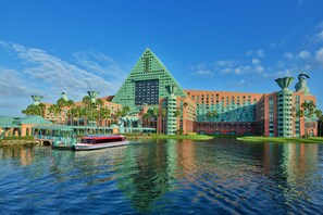 A large hotel with a pyramid-shaped building, a boat on the water, and palm trees. - Walt Disney World Swan (Lake Buena Vista)
