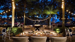 An outdoor dining area with a long table set for a meal, surrounded by chairs, and decorated with string lights and candles. - Walt Disney World Swan (Lake Buena Vista)