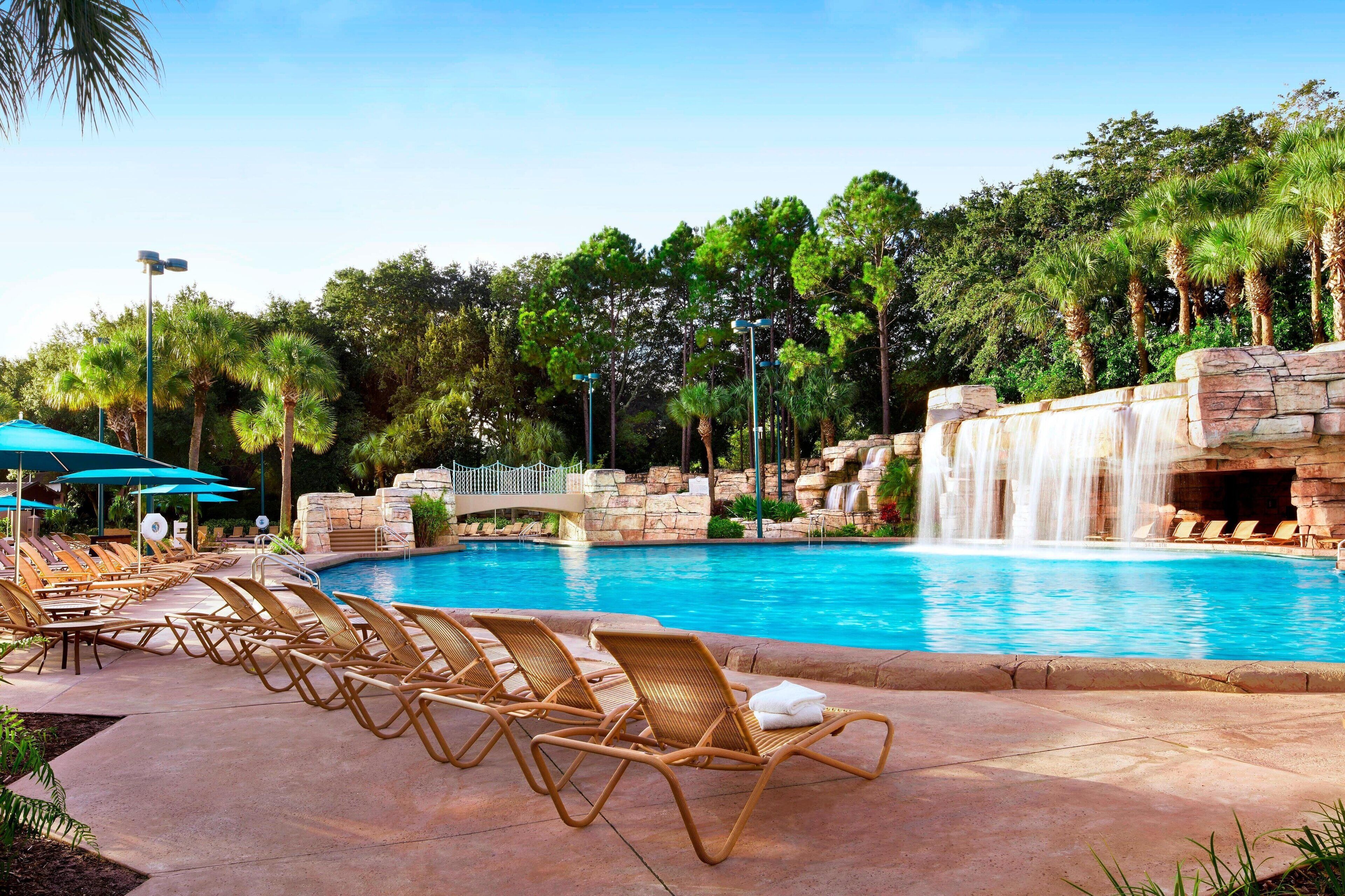 A pool area with lounge chairs, a waterfall, and palm trees.