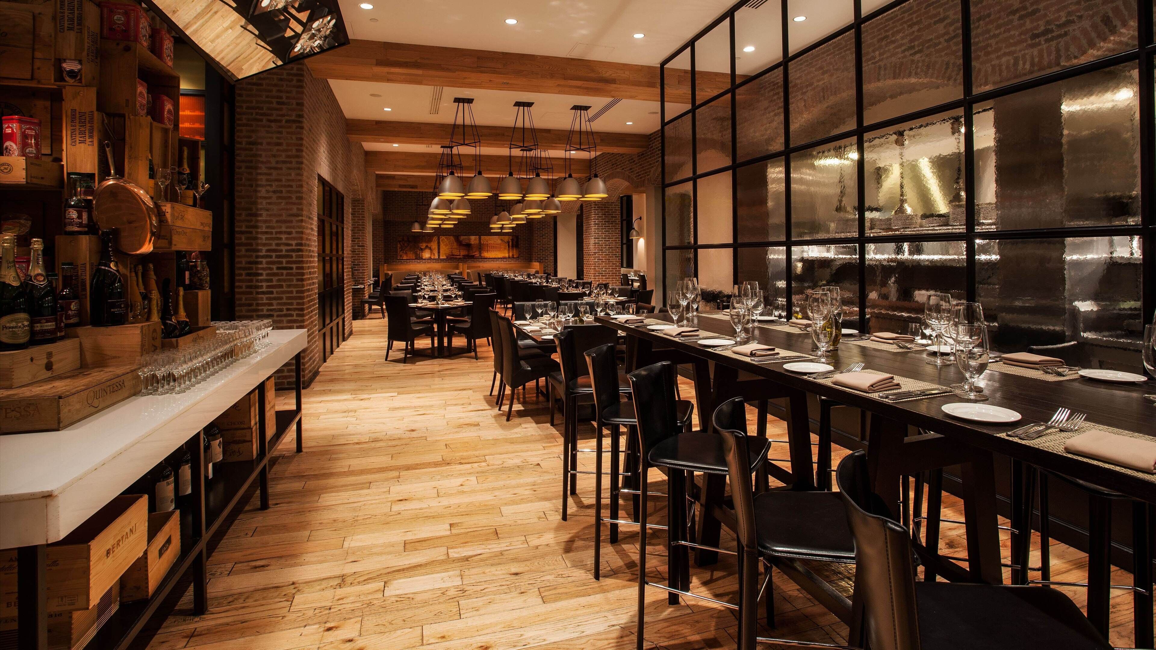 A restaurant with wooden flooring, black chairs, and tables set with wine glasses and plates.