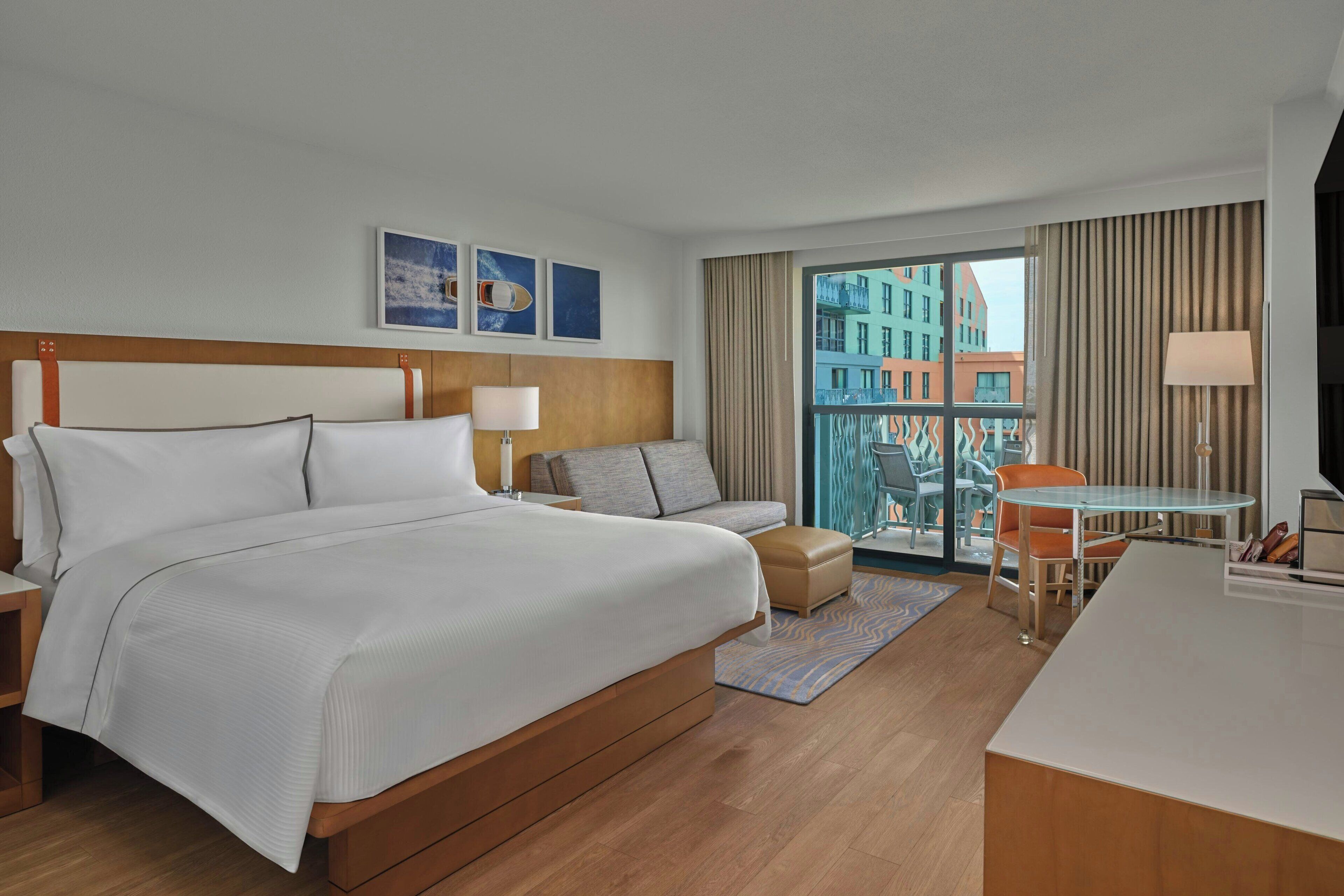 A hotel room with a large bed, a sofa, a desk, and a view of buildings through the window.