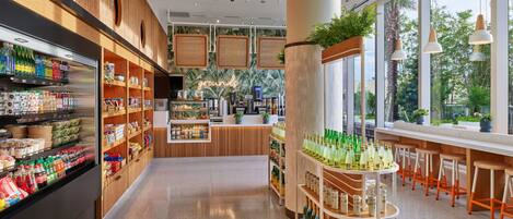 A modern café interior with wooden shelves, a bar area, and large windows offering a view of greenery.