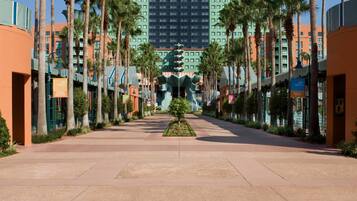 A hotel with a central atrium, palm trees lining the walkway, and a green building in the background.