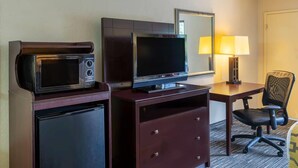 Habitación de hotel con microondas, televisión de pantalla plana, escritorio con lámpara, silla y refrigerador pequeño.