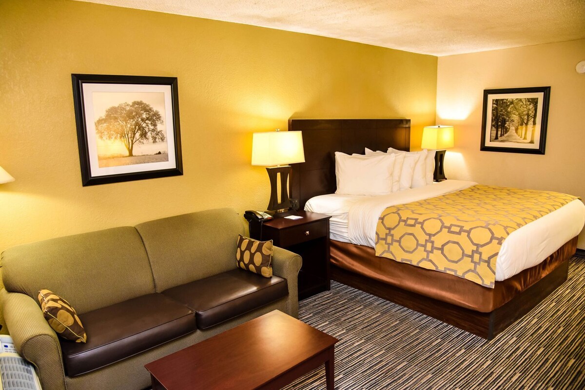 A hotel room with a bed, a sofa, a nightstand, a lamp, and two framed pictures on the walls.