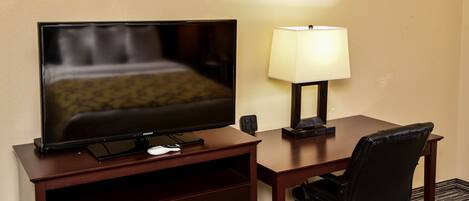 Een hotelkamer met een flatscreen televisie, een bureau met lamp, een stoel en een klein dressoir.