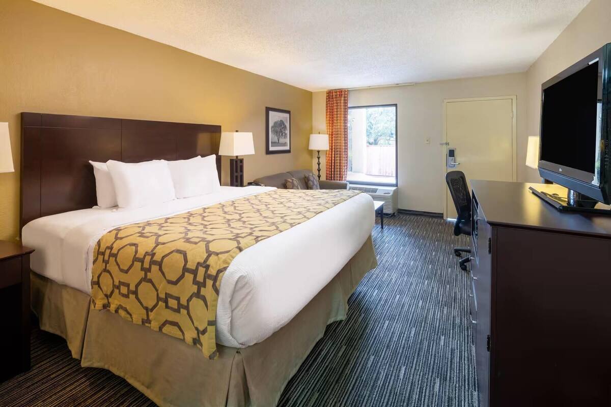 A hotel room with a large bed, a desk with a flat-screen TV, a chair, and a window with curtains.