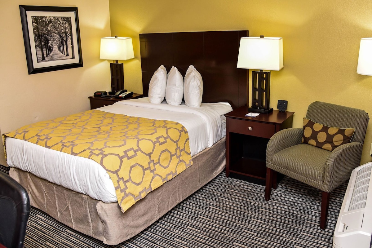 A hotel room with a bed, two bedside tables, a chair, a lamp, a picture on the wall, and a carpeted floor.