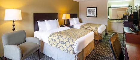A hotel room with two beds, a desk, a chair, a lamp, and a television.