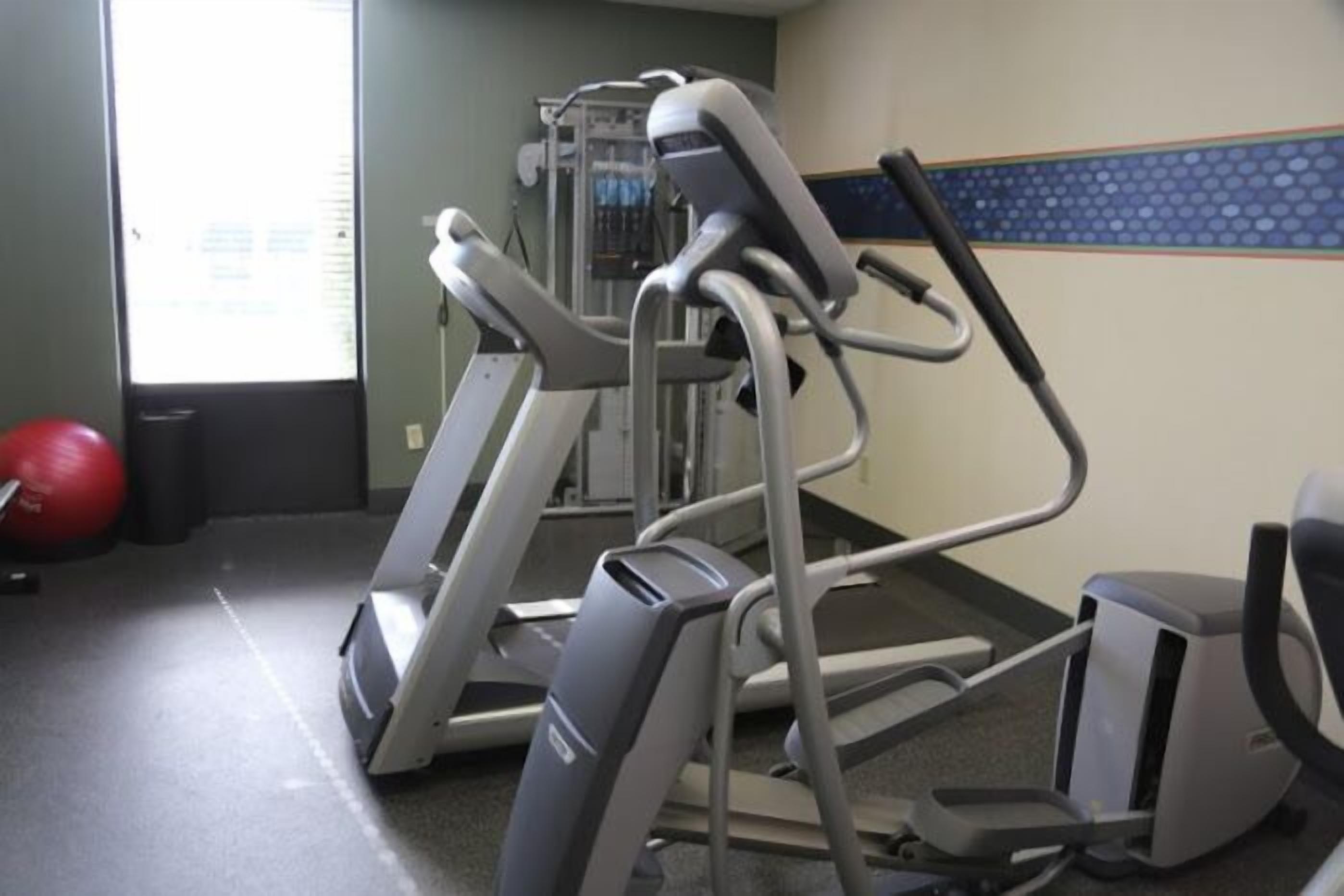 Une salle de sport équipée de tapis de course, d’un vélo d’appartement et d’un ballon d’exercice rouge.