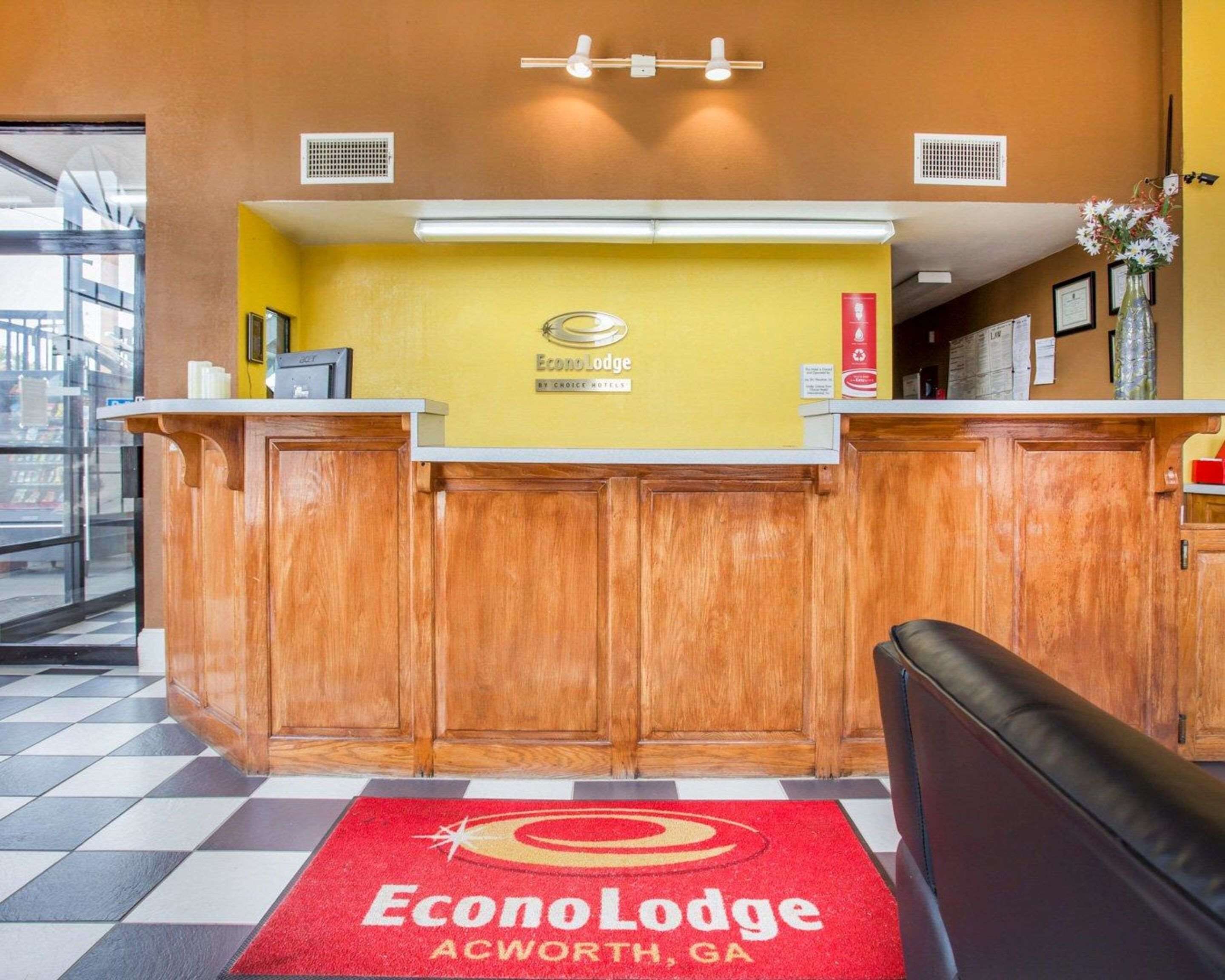 A reception desk at EconoLodge in Acworth, GA, with a check-in counter, a wooden reception desk, a red carpet with the hotel logo, and a wall-mounted sign.
