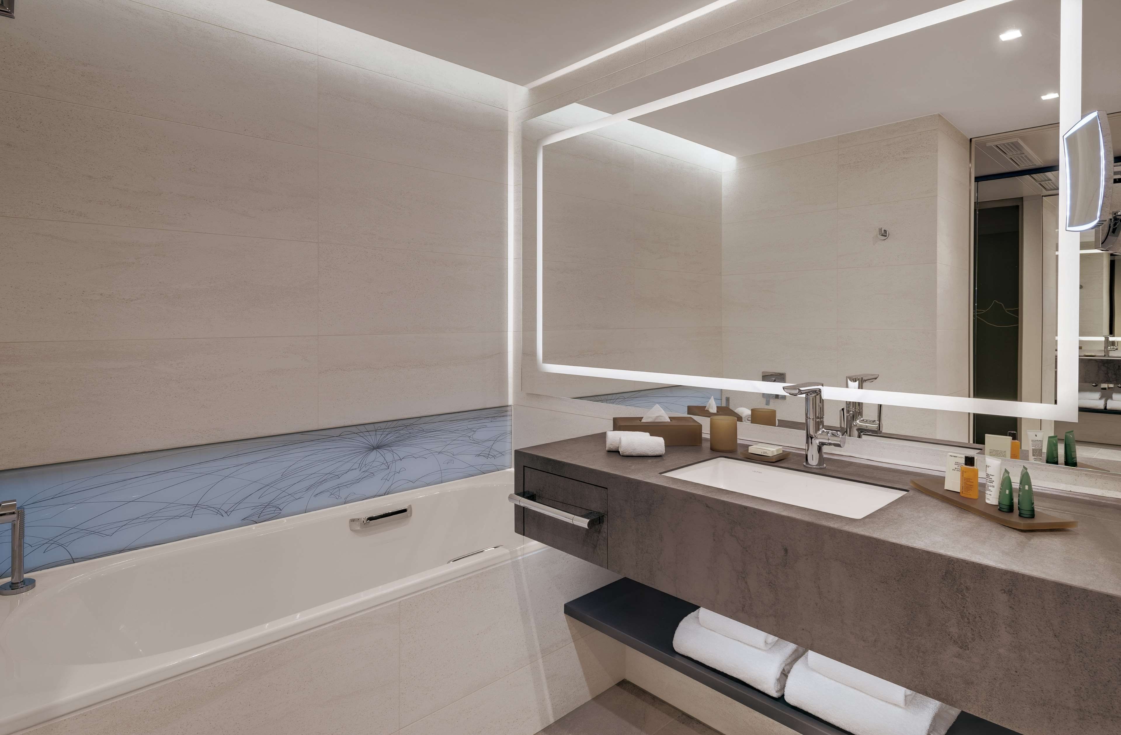 A modern bathroom with a bathtub, a large mirror, and a vanity with toiletries.