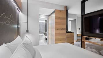 Habitación de hotel moderna con una cama grande, un televisor de pantalla plana, un armario de madera y un baño visible a través de una puerta abierta.