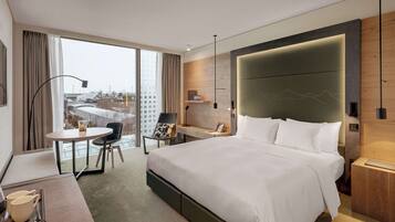 Habitación de hotel moderna con una cama grande, un escritorio, una silla y vistas a la ciudad a través de amplias ventanas.