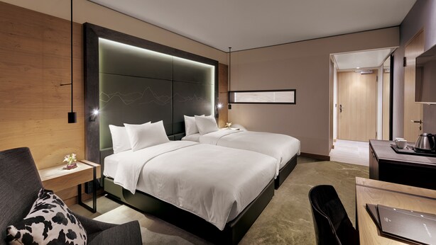 A modern hotel room with two beds, a desk, a chair, and a large mirror.