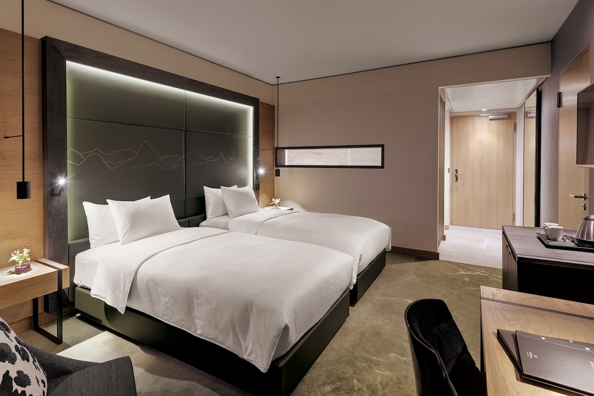 A modern hotel room with two beds, a desk, a chair, and a large mirror.