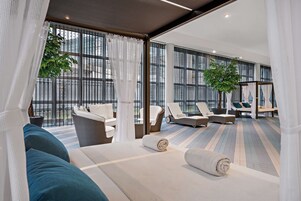 Una habitación de hotel moderna con una cama grande, un área de descanso con sillones y vistas amplias a través de grandes ventanales.