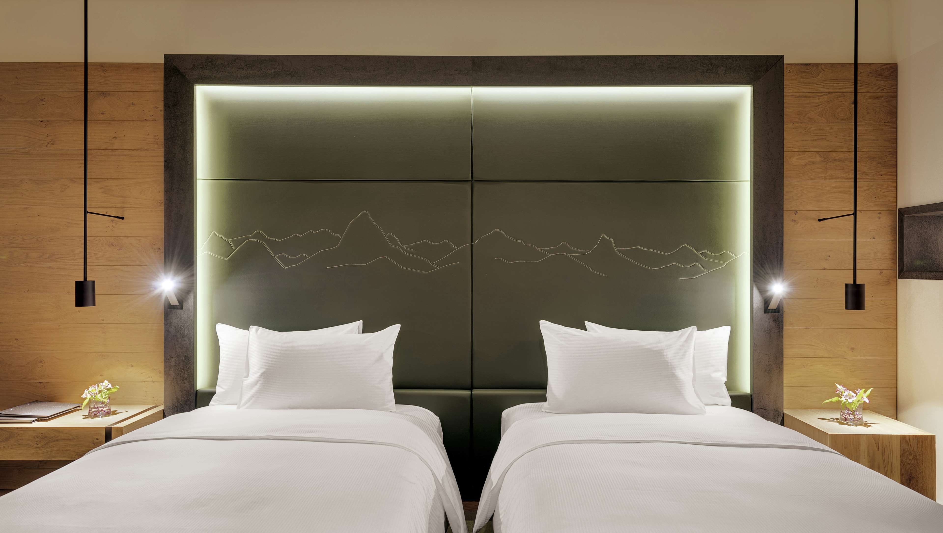 A hotel room with two beds, a large wall-mounted headboard, and a decorative mountain line design.
