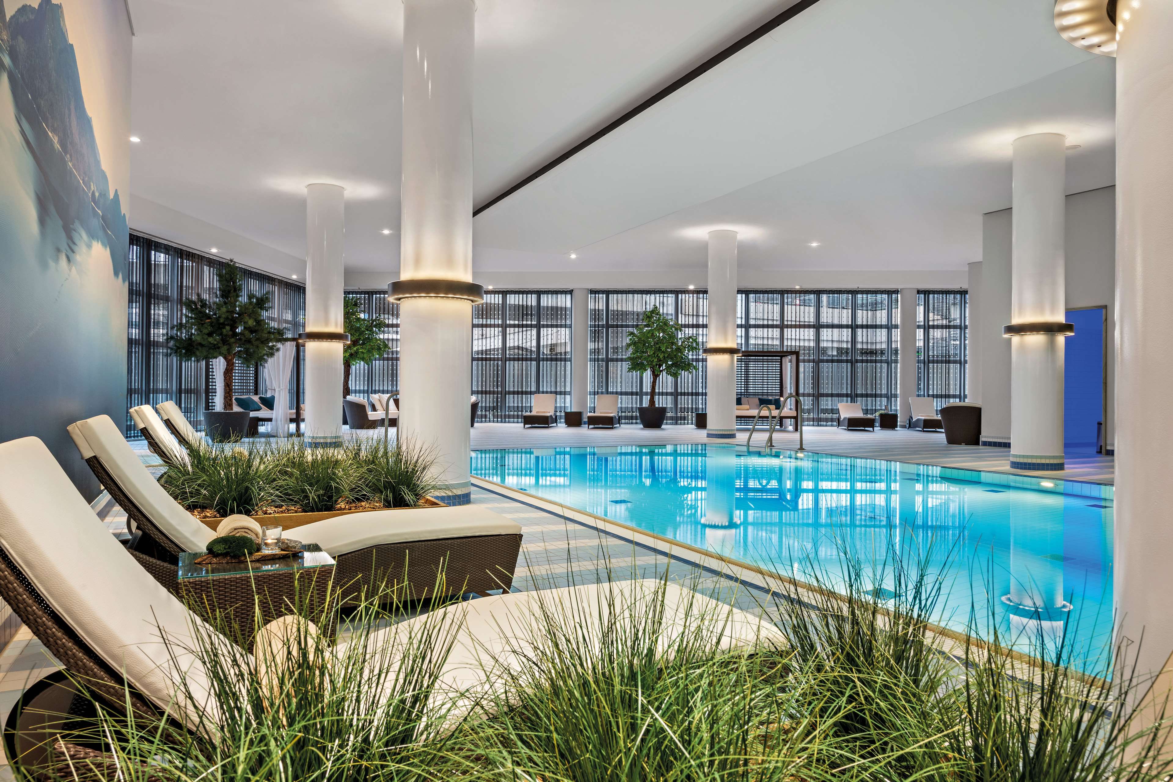 Una piscina interior moderna con sillas de descanso y plantas en macetas.