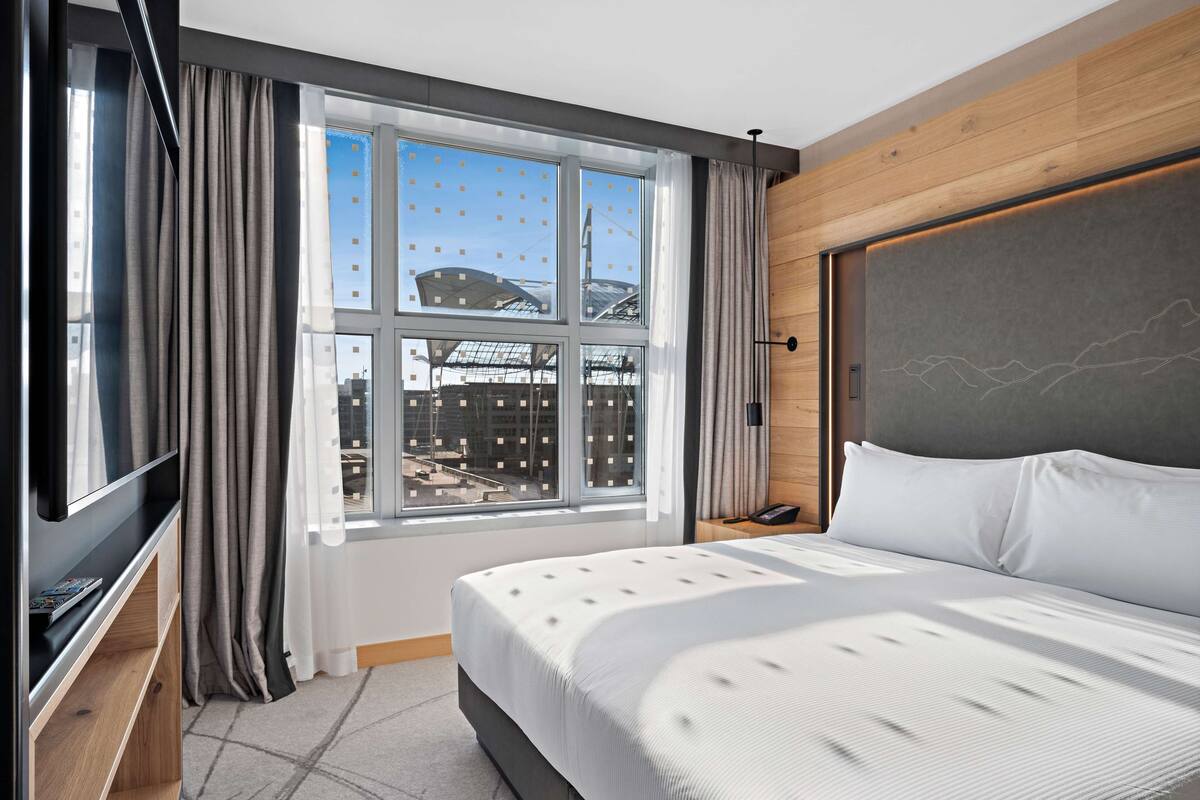 A modern hotel room with a large bed, a TV, and a window with curtains.