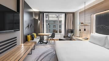 Habitación de hotel moderna con una cama grande, televisor de pantalla plana, mesa de comedor y vistas a la ciudad.