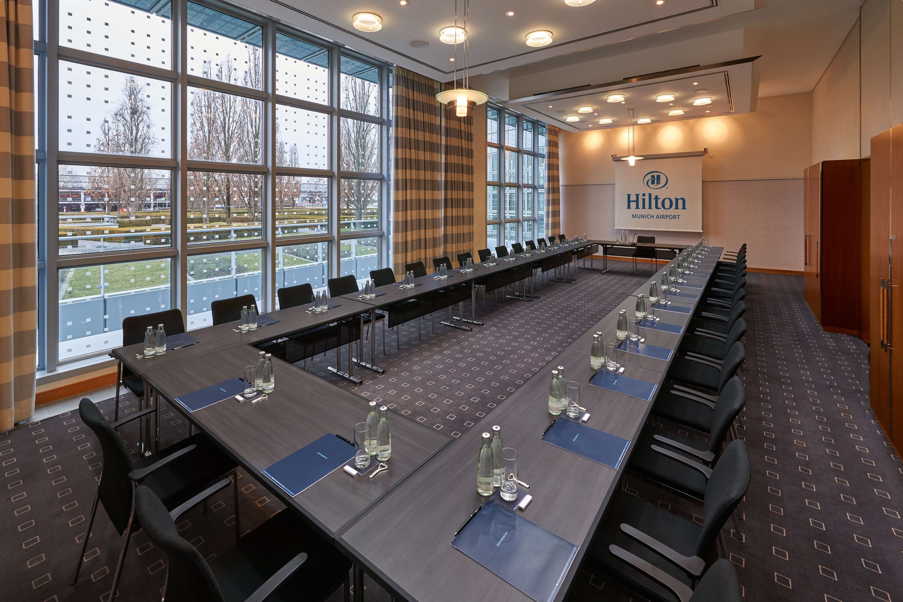 Un salón de conferencias con una larga mesa, sillas y el logotipo de Hilton en la pared.