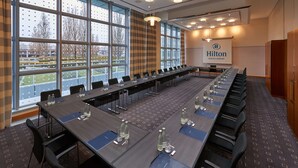 Un salón de conferencias con una larga mesa, sillas y el logotipo de Hilton en la pared.