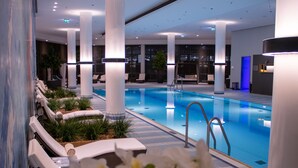 Una piscina interior moderna con sillones blancos de descanso y piso de azulejos azules.