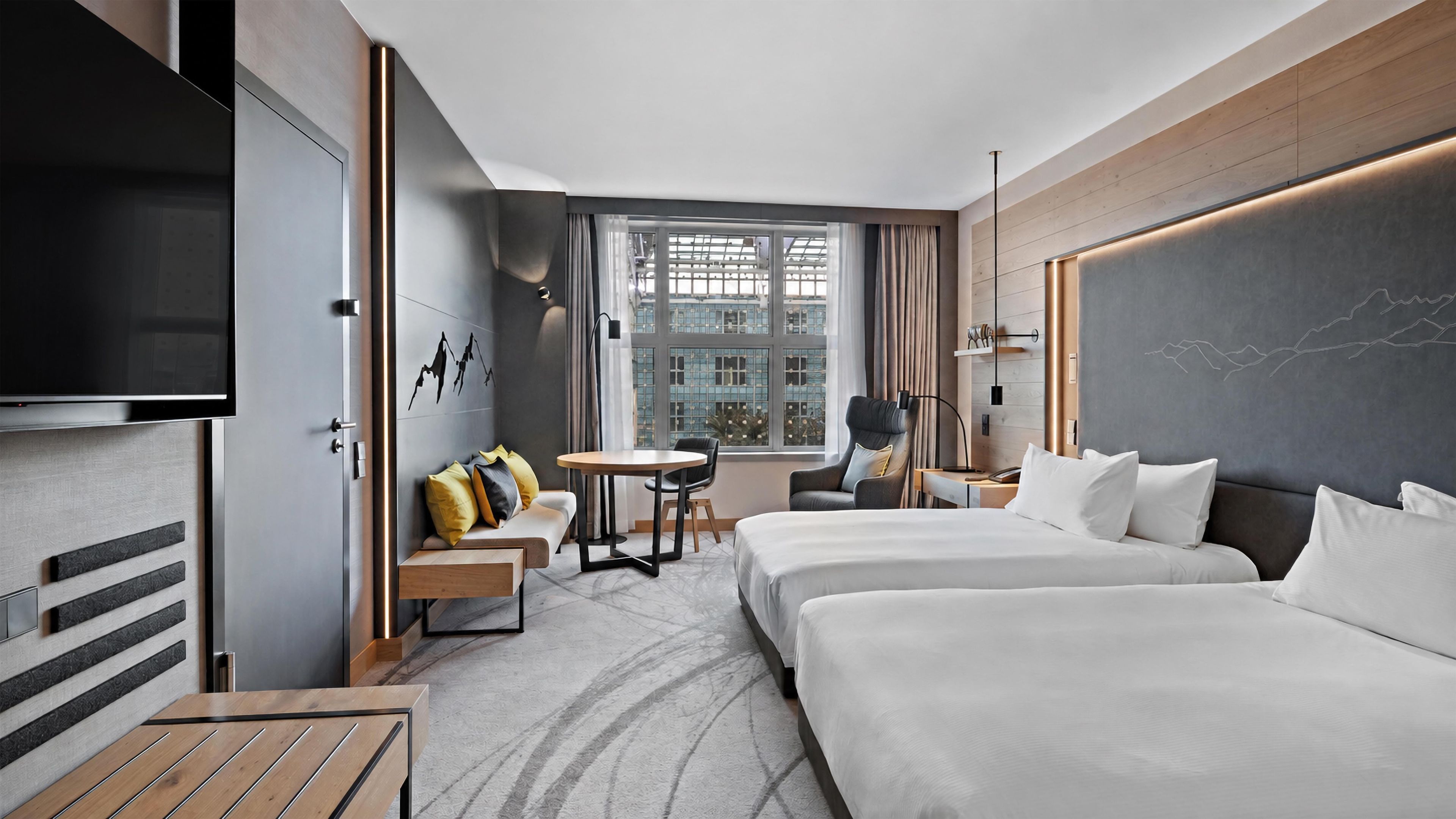 Habitación de hotel con televisión, dos camas, un sofá, una mesita y vistas a la ciudad.