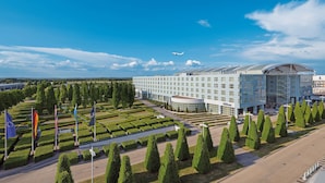 A modern hotel with a glass facade, surrounded by a well-manicured garden and several flags.