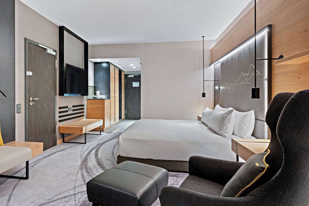 A modern hotel room with a bed, a desk, a chair, and a sofa.