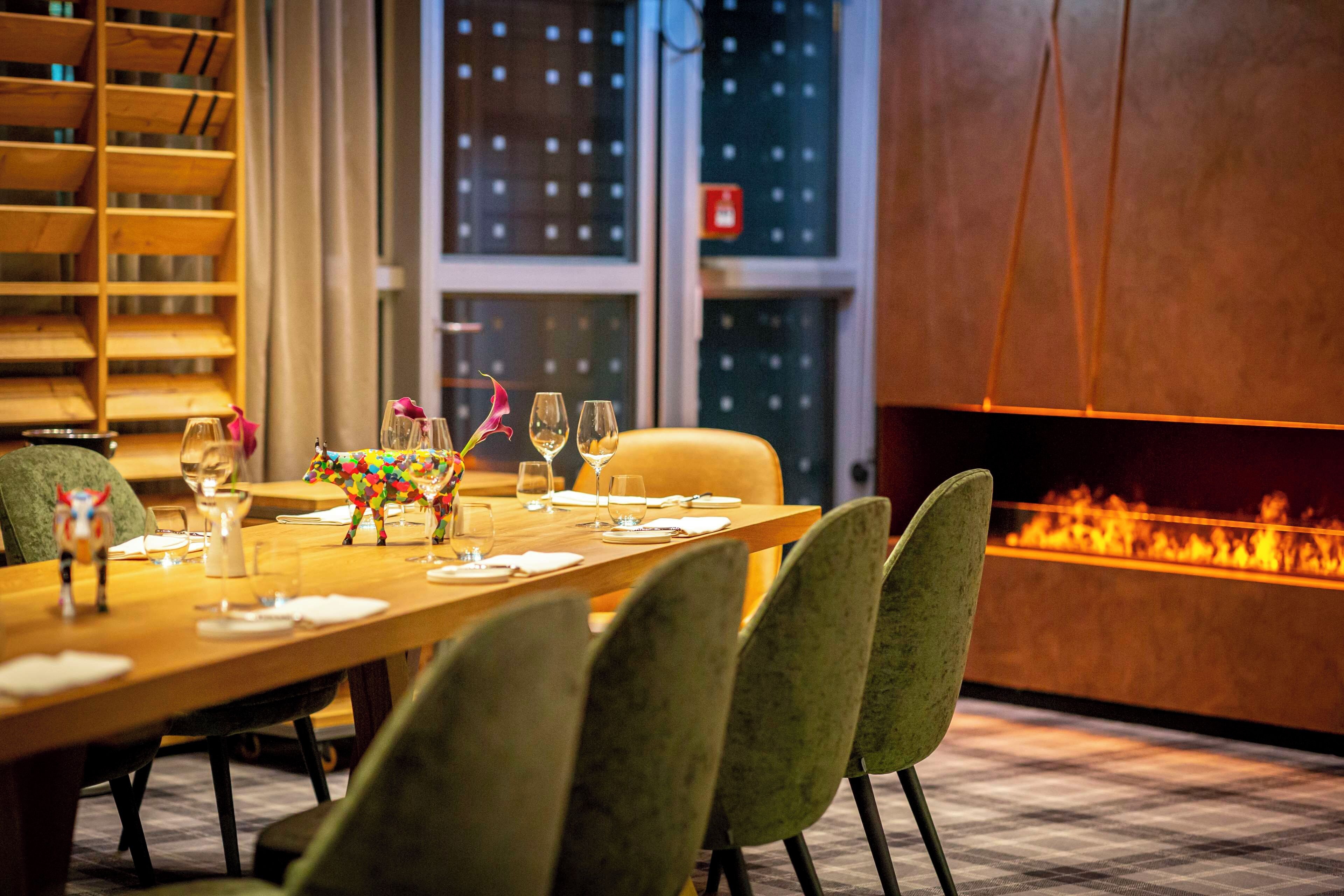 A dining table set with chairs, a decorative animal figurine, wine glasses, and a fireplace.