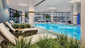 Un área de piscina interior moderna con sillones de descanso, ventanas amplias y pilares decorativos.