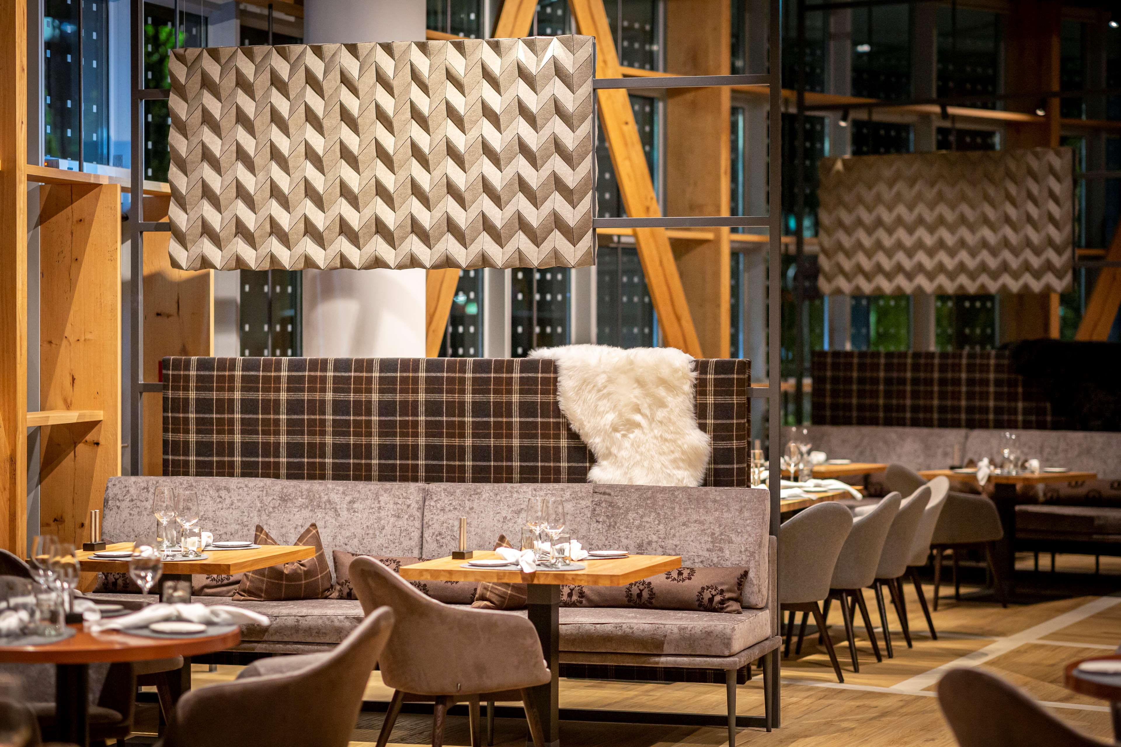 Interior de restaurante con diseño moderno, que presenta una zona central de asientos con una pared con motivos, vigas de madera y una mezcla de asientos tapizados y acolchados.