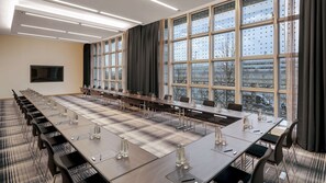 Un salón de conferencias con una larga mesa, sillas y grandes ventanales que ofrecen vista a la ciudad.