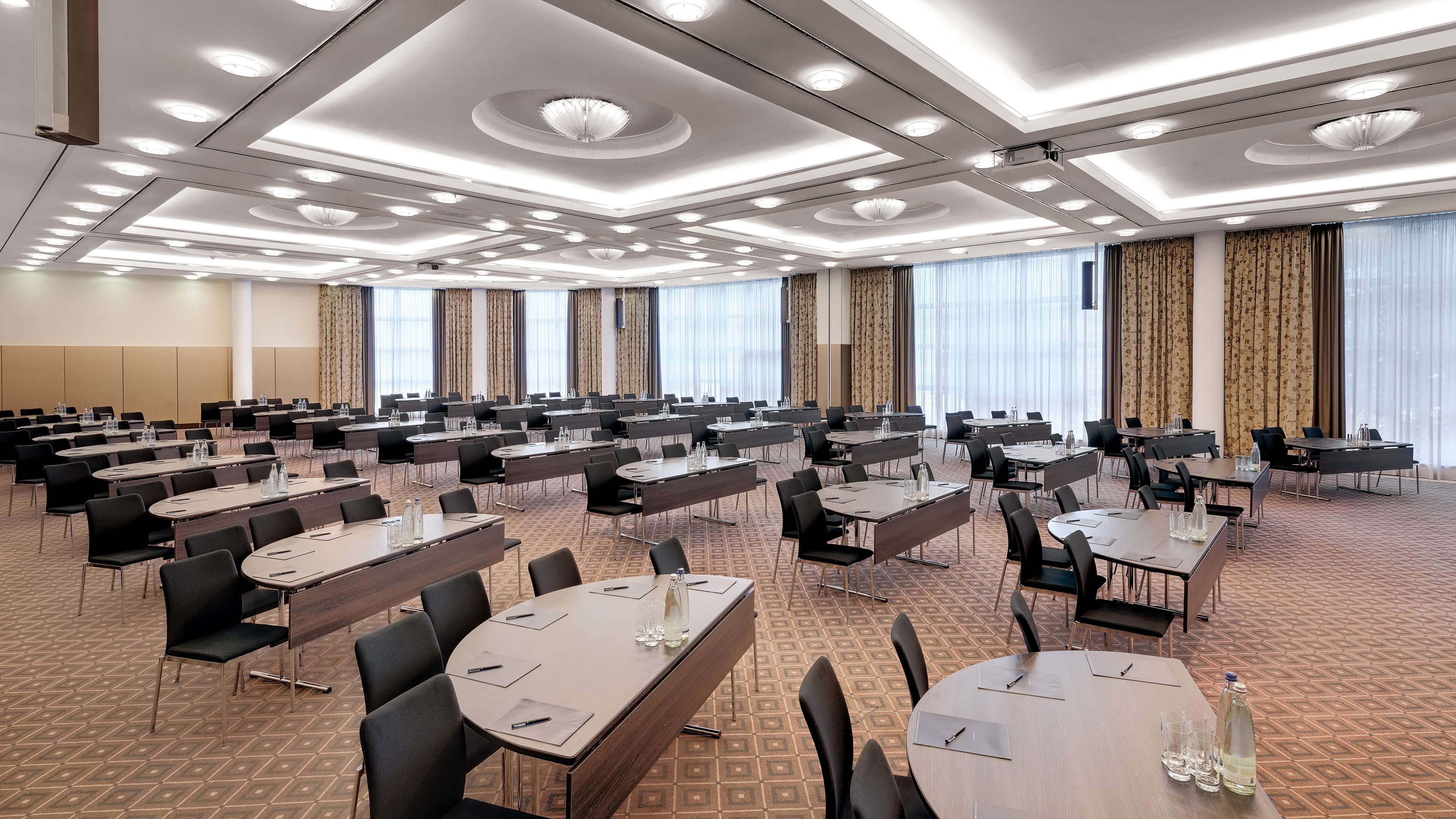 A conference room with multiple tables and chairs, large windows with curtains, and a patterned carpet.