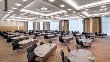 Un salón de conferencias con varias mesas y sillas, ventanas amplias con cortinas y una alfombra estampada.